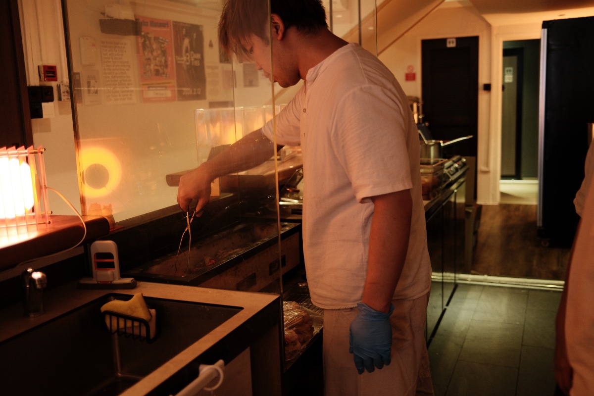 Caleb Ang cooking the burger patty over a charcoal grill. (Photo Credit: Jaclene Liew)